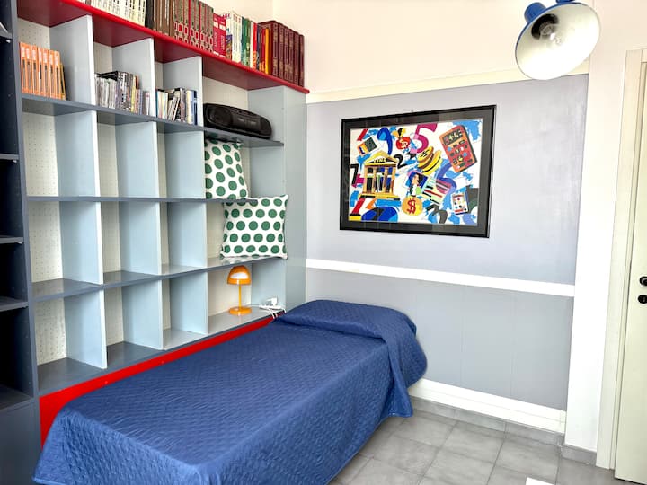Светла и функционална еднокреветна соба, со единечен кревет, интегриран ѕид со полица за книги и декорации со поп-арт