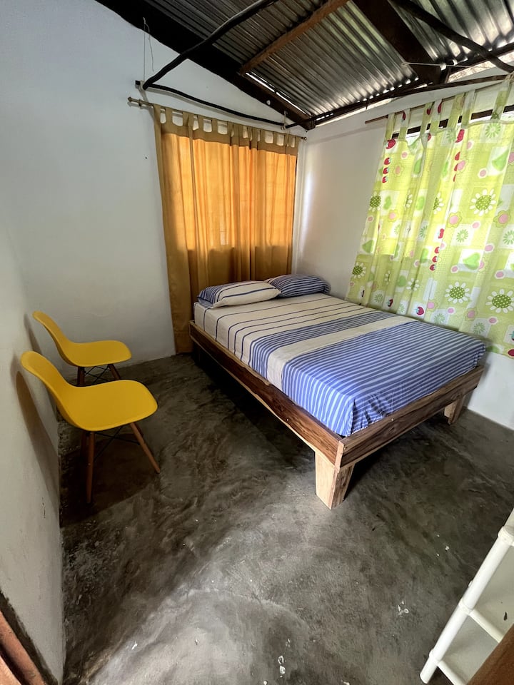 Habitación 3:  sencilla, con cama doble en base de madera, cortinas coloridas y sillas. Cuenta con soporte para instalar el toldillo y ventilador de pared, ideal para un descanso cómodo y protegido en medio del ambiente natural de Palomino.