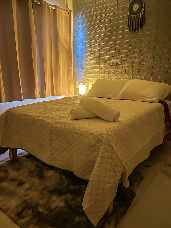 ACOGEDORA RECAMARA QUE CUENTA CON CAMA MATRIMONIAL, BURO Y LAMPARA DE NOCHE