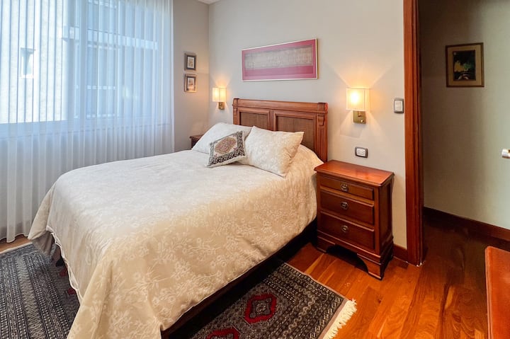 Una cama tamaño queen, sábanas de algodón egipcio de lujo y almohadas generosas te invitan a dormir. La iluminación cálida crea un ambiente íntimo y relajante, perfecto para leer o compartir momentos especiales.  