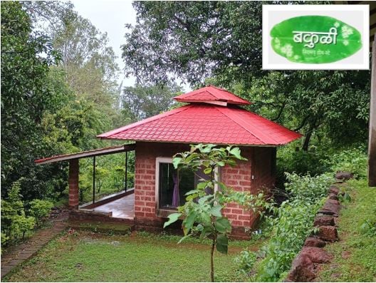 A rustic cottage is framed by lush greenery, featuring a red tiled roof and brick walls. A spacious porch extends from the entrance, offering a view of the surrounding natural landscape. The scene is enhanced by the tranquil atmosphere of the area.