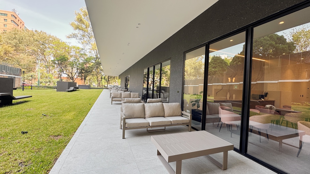 An outdoor terrace area is presented, featuring several soft seating arrangements on a spacious patio. Large sliding glass doors provide a view into the indoor space. Lush greenery surrounds the terrace, complementing the tranquil atmosphere.