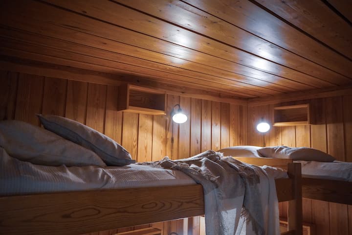 Varm och inbjudande sovplats med robusta 100 cm breda våningssängar, mjuk belysning och naturlig träomgivning – ett mysigt och säkert utrymme för barn eller vänner att vila och ladda upp.