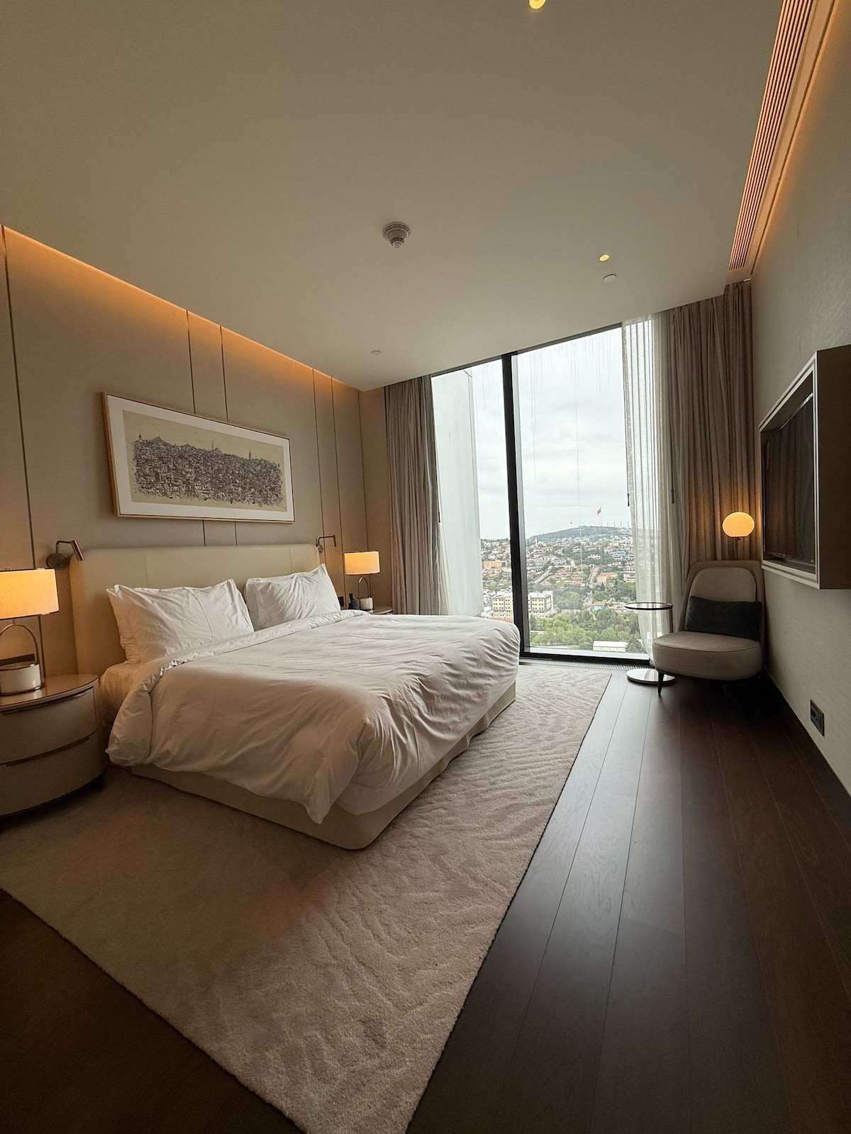 Dormitorio sereno con una cama king, iluminación suave y vistas panorámicas a la ciudad a través de las ventanas del piso al techo.