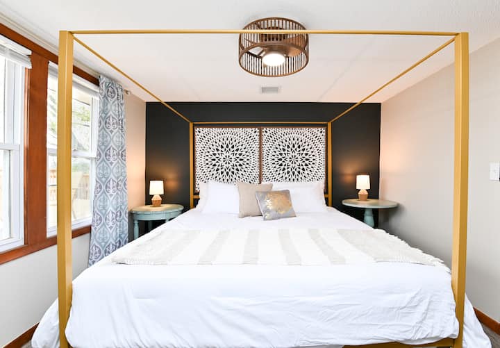 Mpangilio wa kitanda cha kifuniko cha kifalme ulio na taa za kusomea, meza za kuweka vitu na televisheni janja ya Roku ya inchi 42.