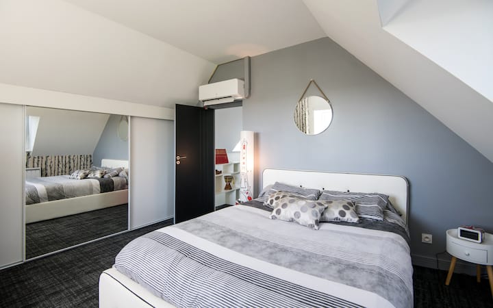 A l'étage : chambre moderne aux tons gris et blanc, dotée d’un lit 160 cm et d’un grand rangement. Climatisée, elle offre une vue apaisante sur la campagne.