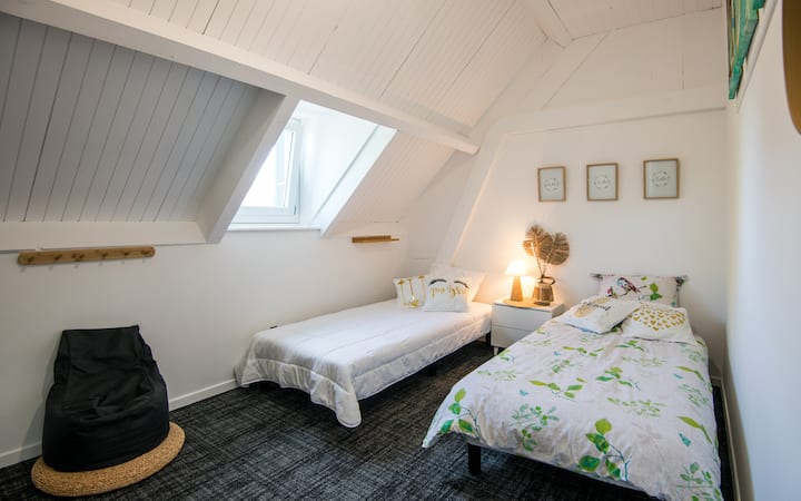 À l'étage : chambre cosy climatisée avec deux lits 90 cm, coin bureau et rangement. Baignée de lumière grâce à sa lucarne, elle offre une ambiance douce et reposante. 
Parfaite pour enfants, amis ou frères & sœurs en quête de confort et de calme.