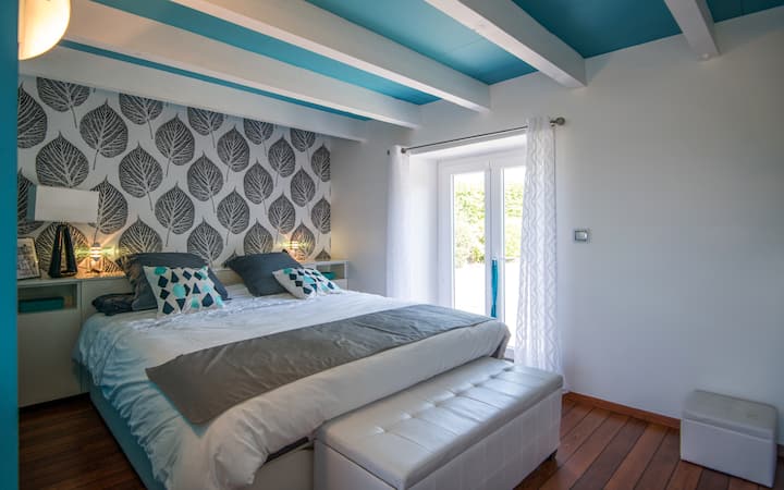 Suite parentale de 24 m² au rez-de-chaussée, avec lit 180 cm, îlot central de rangement dissimulant une télévision, baignoire, douche, vasque et grands rangements. Trois fenêtres apportent une belle lumière naturelle.
Un espace élégant et intime.