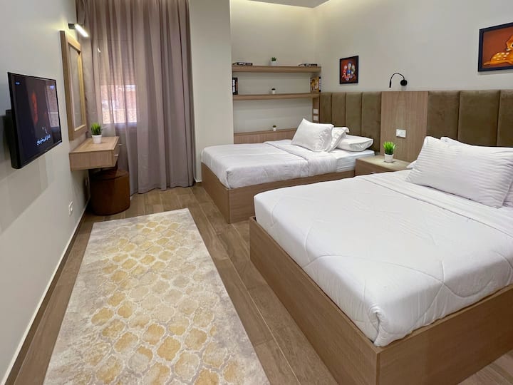 غرفة نوم مريحة تضم سريرين مفردين، فرش عالي الجودة، أثاث أنيق، ديكور هادئ، إضاءة ناعمة، بياضات نظيفة، ستائر فاخرة، سجاد أرضيات أنيق، وشاشة مسطحة لضمان راحة واستمتاع الضيوف