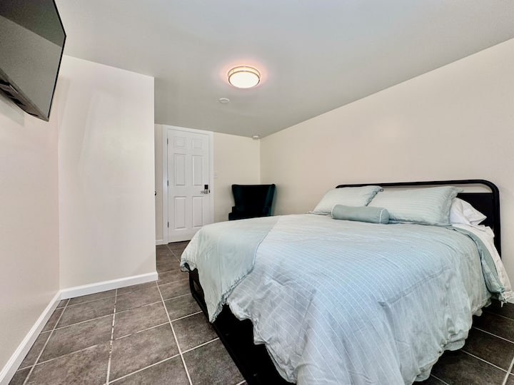 Ფართო საძინებელი Queen-ის საწოლით, სმარტ-ტელევიზორითა და მყუდრო სამკითხველო სკამით.