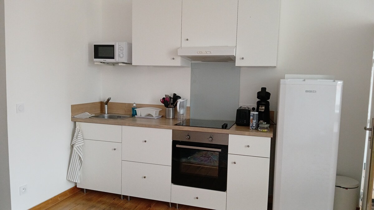 A modern kitchen setup features sleek white cabinetry and a combination of essential appliances, including a microwave, oven, and refrigerator. Counter space is provided for food preparation, with kitchen utensils and a coffee maker visible on the countertop.
