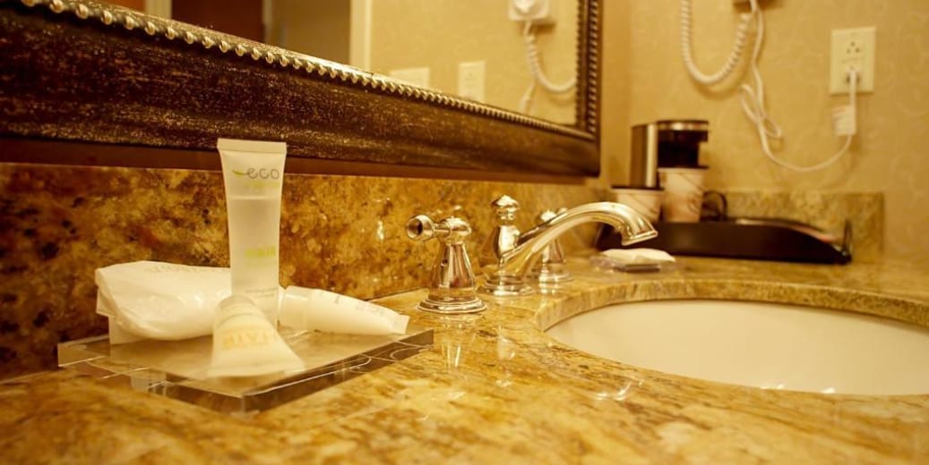 A well-appointed bathroom vanity features a sleek countertop with a variety of personal care items arranged neatly. A modern faucet complements an elegant sink, while a decorative mirror adds depth to the space. Amenities include complimentary toiletries and a coffee maker nearby.