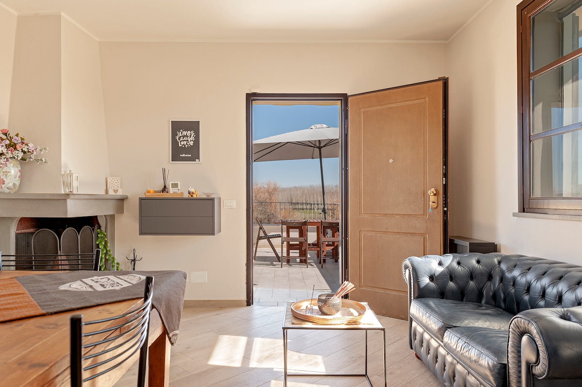 A welcoming living space features a comfortable leather sofa, a wooden dining table, and an open door leading to a patio area. Natural light illuminates the room, while a scenic view of the outdoors is visible through large windows.