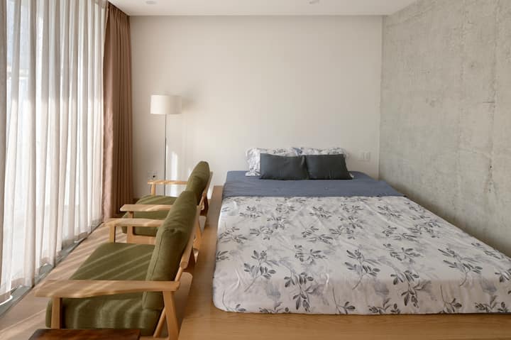 De slaapkamer van️ kamer 301 heeft een zacht bloemenbed, twee olijfgroene fauteuils en een eenvoudige vloerlamp ☀️ – perfect om te genieten van het zonlicht of om te ontspannen met een boek.