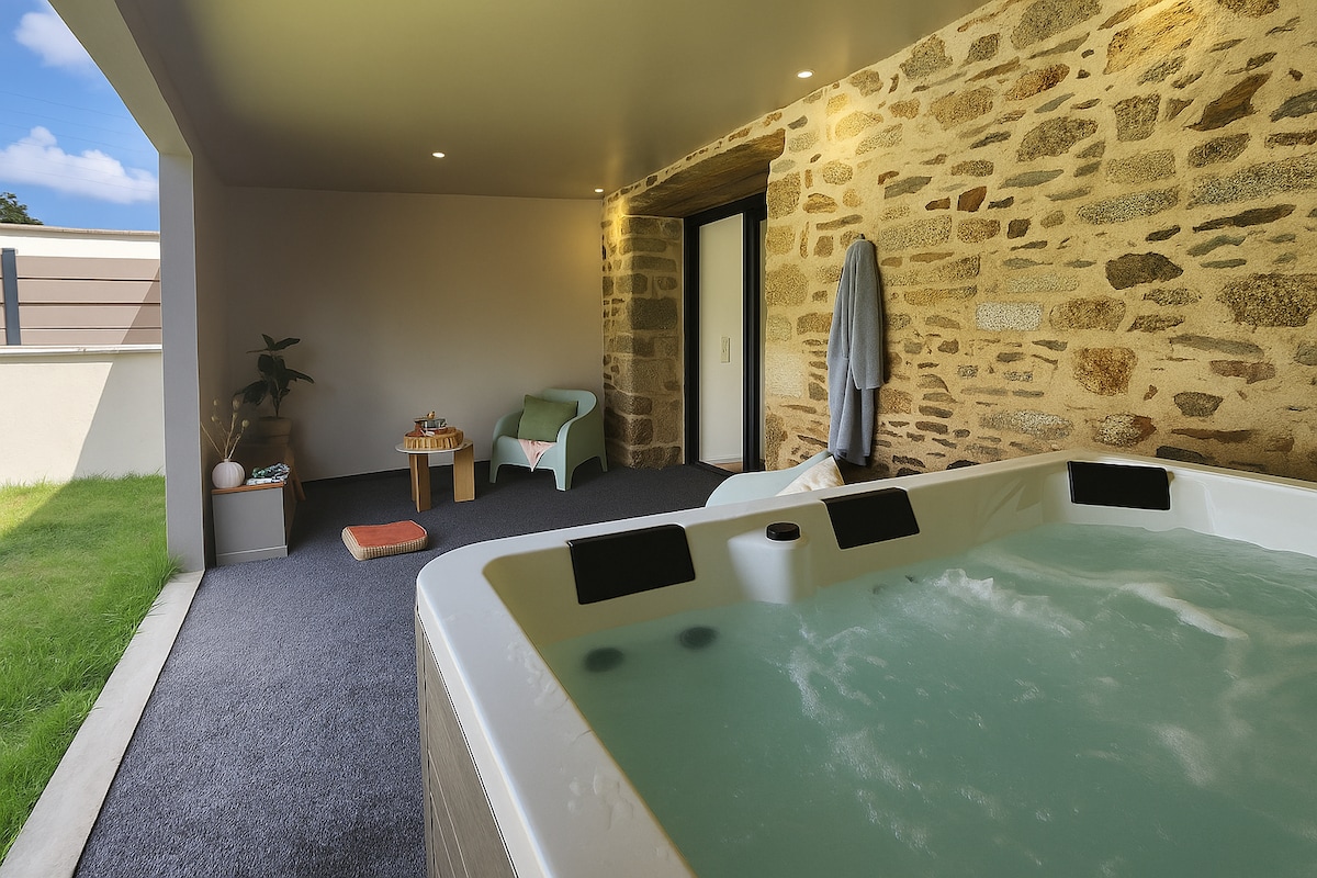 A relaxing spa area features a hot tub with bubbling water, surrounded by stone walls. A green lounge chair and a small table are situated nearby, while a towel hangs on a hook. Soft lighting enhances the tranquil environment.