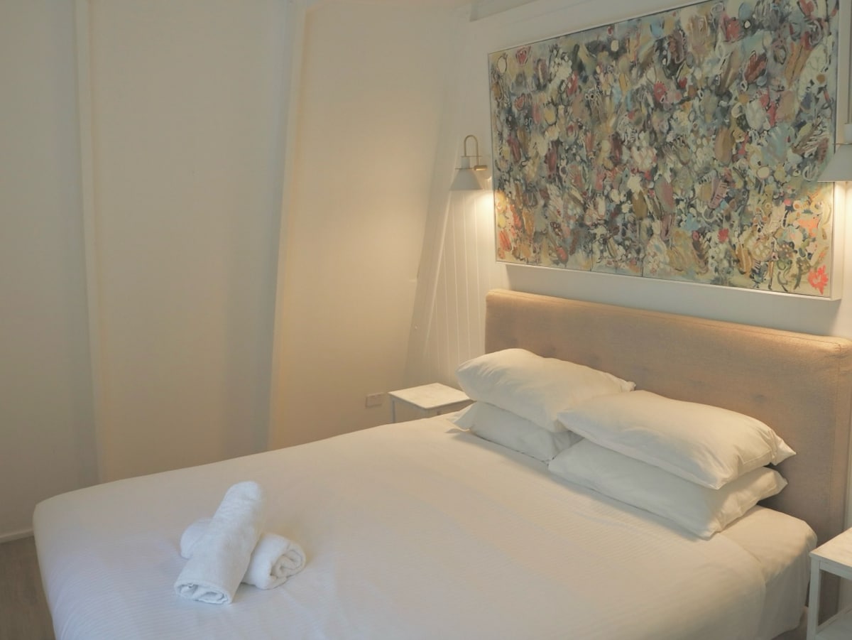 Spálňa 2 – Ružová izba (hore, manželská posteľ)
Tienený úkryt orámovaný pôvodnou zeleňou a teplým bielym drevom. Zemitá paleta sa stretáva s uvoľneným, rafinovaným štýlom.

