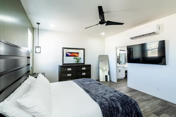  استرخ على السرير الفاخر بحجم كبير مع فراش فاخر في غرفة النوم الرئيسية الفسيحة، مع تلفزيون 65 بوصة للترفيه.