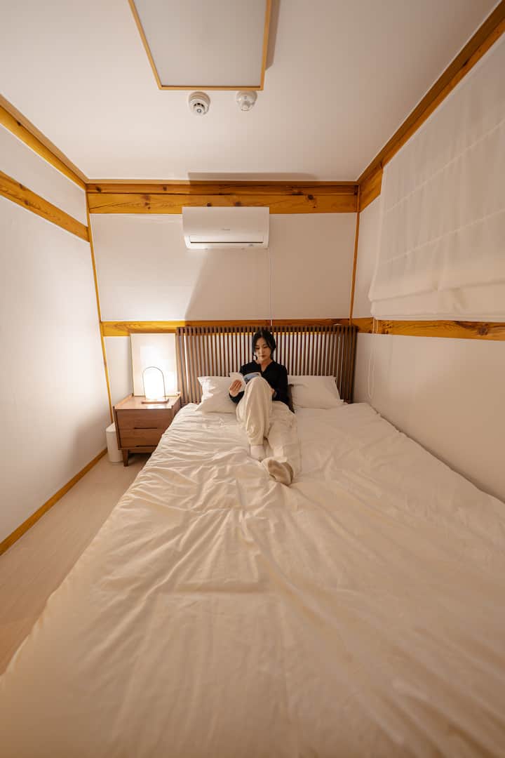 Спокойният комфорт на малка стая.
Потопете се в уютното легло под меката светлина и напрежението от деня ще се стопи.
Звукът на вятъра през прозореца и деликатния аромат на дърво
Това е място, където дори звукът на книга е обгърнат с топлина.
Не е голямо, така че е по-уютно и времето е изцяло ваше.