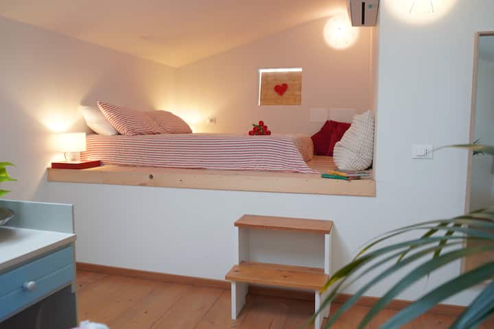 Chambre au dernier étage, ouverte sur l'espace ouvert, avec un lit double romantique surélevé. La chambre comprend une armoire murale, un bureau et une télévision intelligente.
