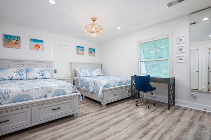 - Пространа гостинска соба со два брачни кревета и мека сина крајбрежна постелнина за удобност
- Големиот прозорец пропушта природна светлина, а бирото со морнарски стол е совршено за работа
- Врамените отпечатоци од плажа, осветлувањето на лустерот и фиоките за складирање го комплетираат поставувањето