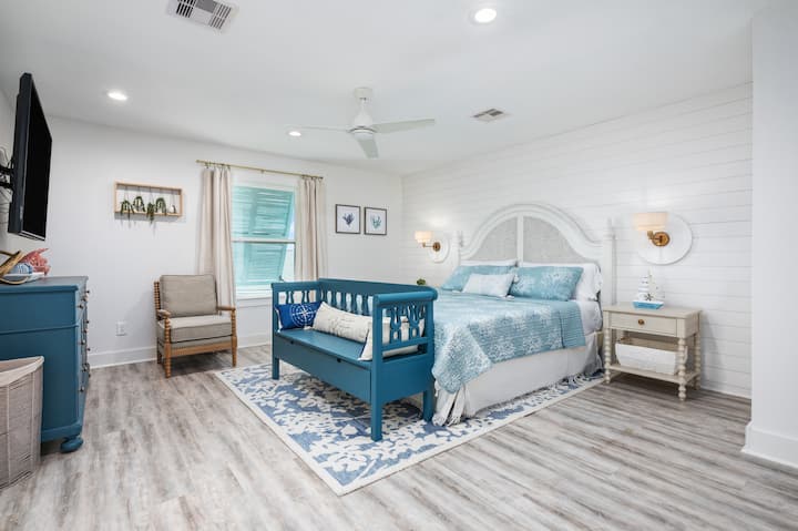 - Спокојната брачна спална соба има меки океански нијанси, елегантна табла на глава и стилско осветлување
- Декоративната клупа во подножјето на креветот додава шарм и практично седење
- Ѕидот со акцент на шиплап, уметноста на плажа и удобните текстури создаваат мирно место за одмор