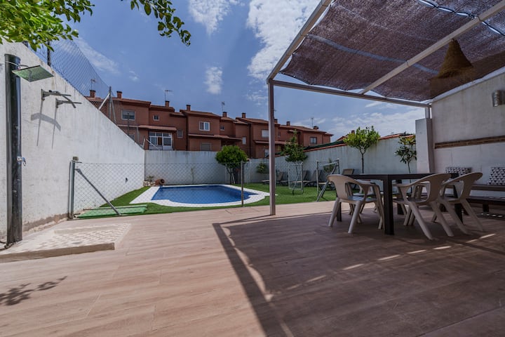 Pérgola con mesa exterior junto a la piscina.