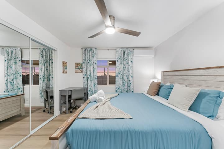 Оваа елегантна спална соба има рустикален дрвен кревет со сина прекривка за кревет, беж фрлање и соодветна ноќна масичка. Огледален плакар, додека сиво биро со телевизор и монитор создава работен простор. Тавански вентилатор, клима уред и природна светлина обезбедуваат удобност.