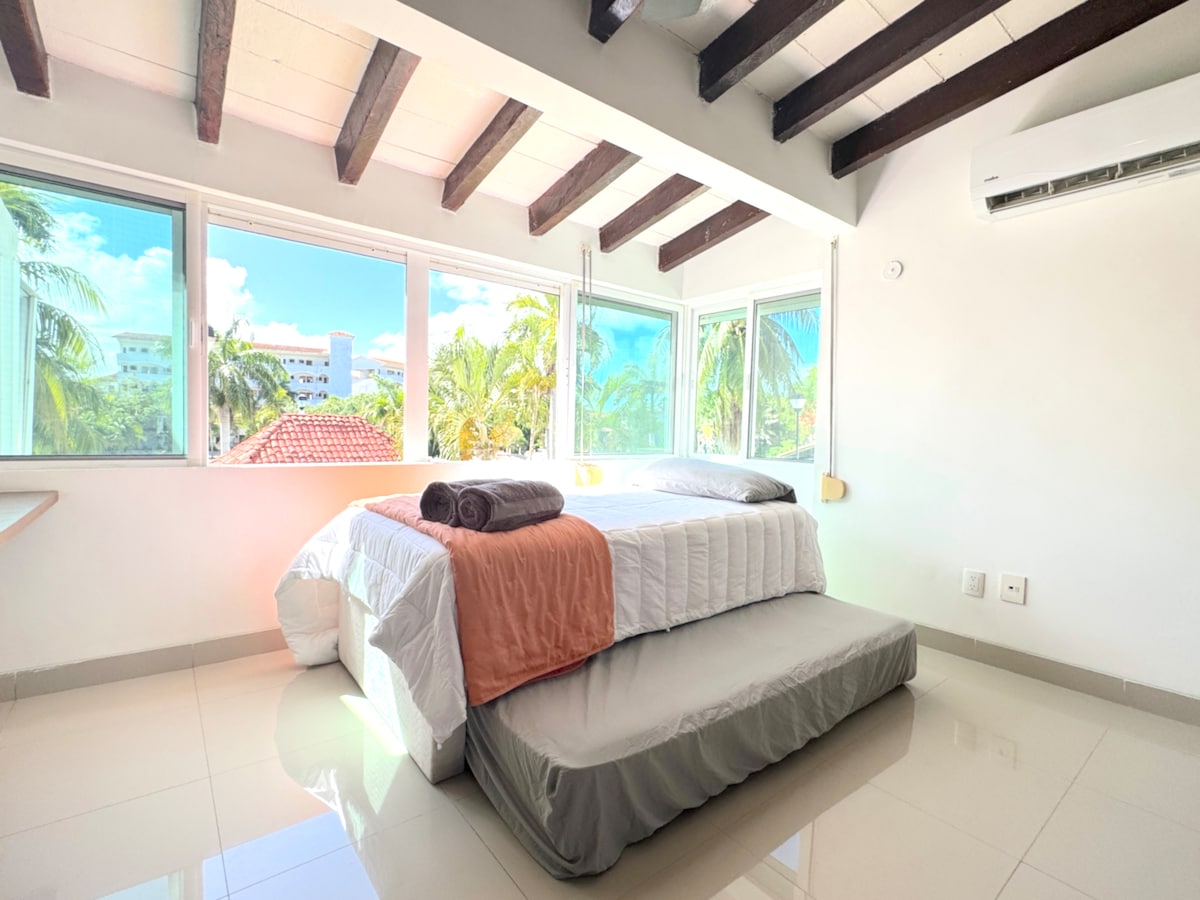 ห้องมุมโปร่งโล่งมีหน้าต่างบานใหญ่พร้อมวิวเขตร้อนคานที่เปิดโล่งและการจัดที่นอนที่ยืดหยุ่น