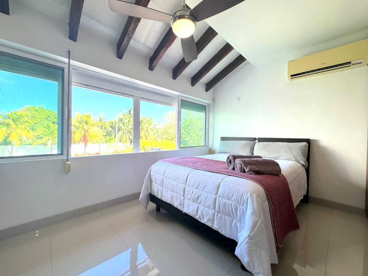 ห้องนอนที่สว่างสดใสและอบอุ่นพร้อมเตียงควีนไซส์ที่สะดวกสบายเพดานโค้งและหน้าต่างบานใหญ่ที่มองเห็นวิวสวนอันเขียวชอุ่มพร้อมห้องน้ำในตัวส่วนตัว