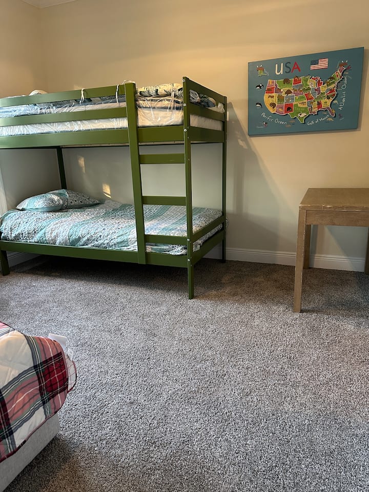 Slnečná a jednoduchá spálňa s dvojlôžkovými poschodovými posteľami a dvojlôžkovou posteľou, písacím stolom na prácu alebo štúdium, stropným ventilátorom na udržanie chladu a mini zásuvkou na odloženie vecí – ideálne na prácu alebo oddych.