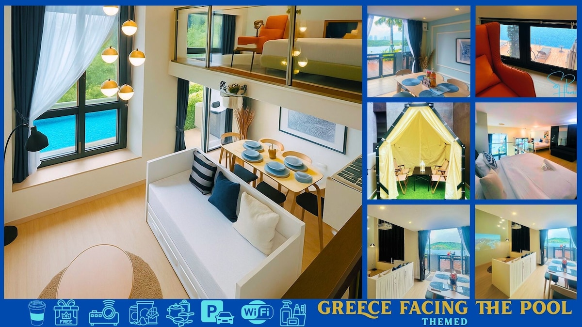 An open-concept loft space features a white sofa positioned near a round coffee table, with a dining setup visible in the background. Large windows frame views of the infinity pool, allowing natural light to fill the area. Relaxing seating options are scattered throughout.