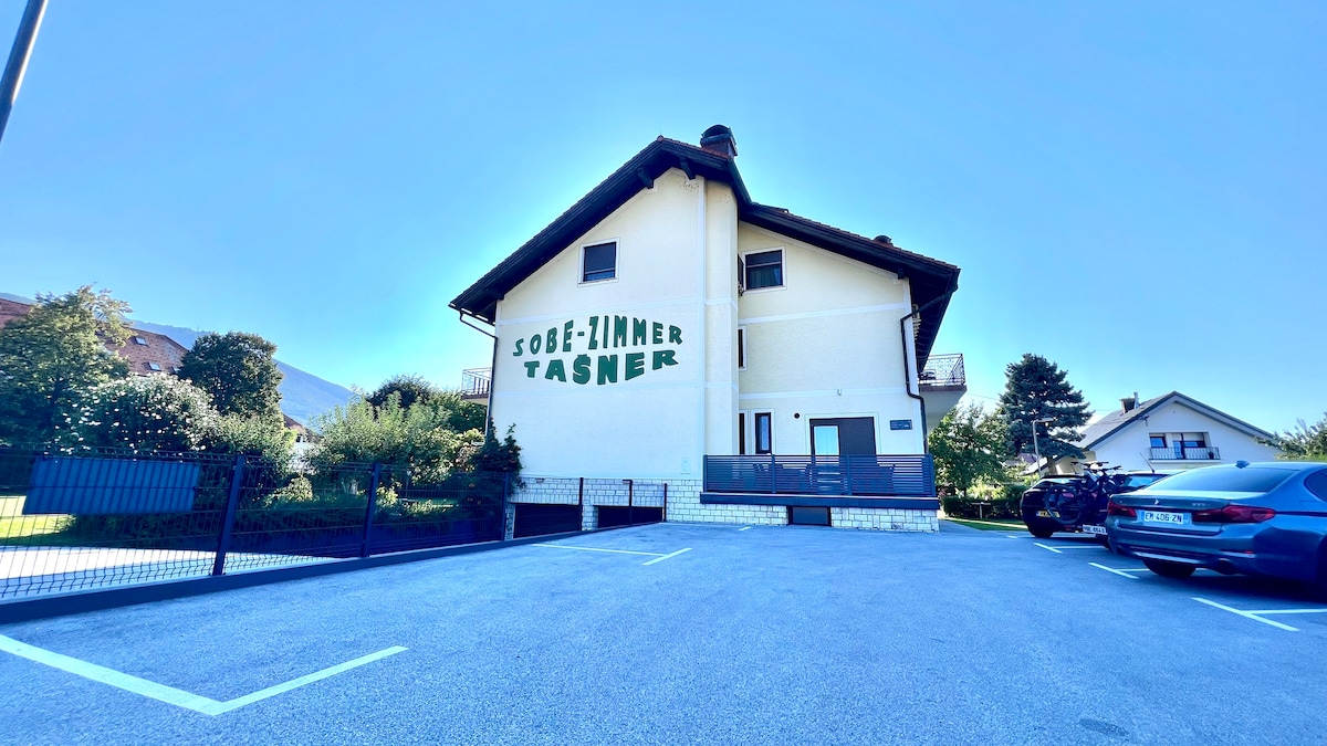 A two-story building is presented, featuring a prominent sign that reads 'SOBE-JIMMER TASNER' on its exterior. A spacious parking area is visible in front, with several parking spaces outlined. Surrounding greenery adds to the serene environment, enhancing the proximity to nature.