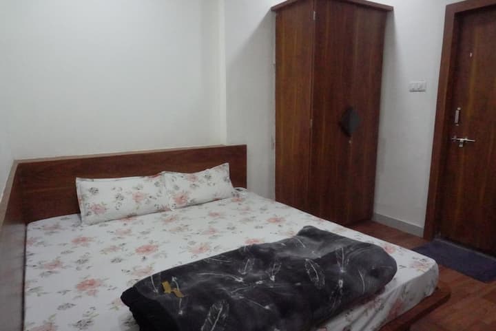 Gezellige slaapkamer met een tweepersoonsbed met bloemen en kussens

Houten hoofdeinde en kledingkast voor een warme uitstraling

Eenvoudige witte muren versterken de helderheid

Compacte, functionele indeling met een strakke uitstraling

Een donkere deken voegt contrast toe aan zachte tinten