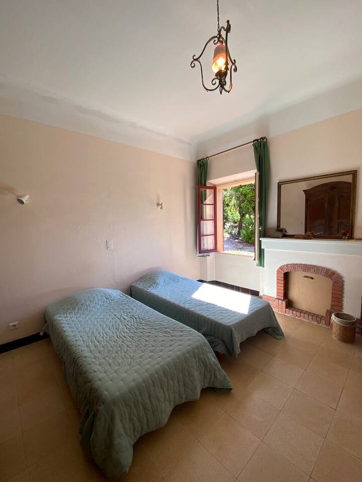 Deux lits simples dans une chambre aux teintes douces, avec une belle fenêtre ouverte sur le jardin. Idéale pour les enfants ou amis, avec un confort simple et agréable.