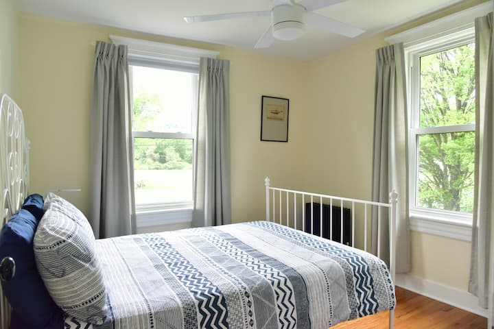 Este dormitorio en el segundo piso tiene una cama completa, ventilador de techo, lámpara de lectura junto a la cama y vestidor con espacio para colgar y estante.