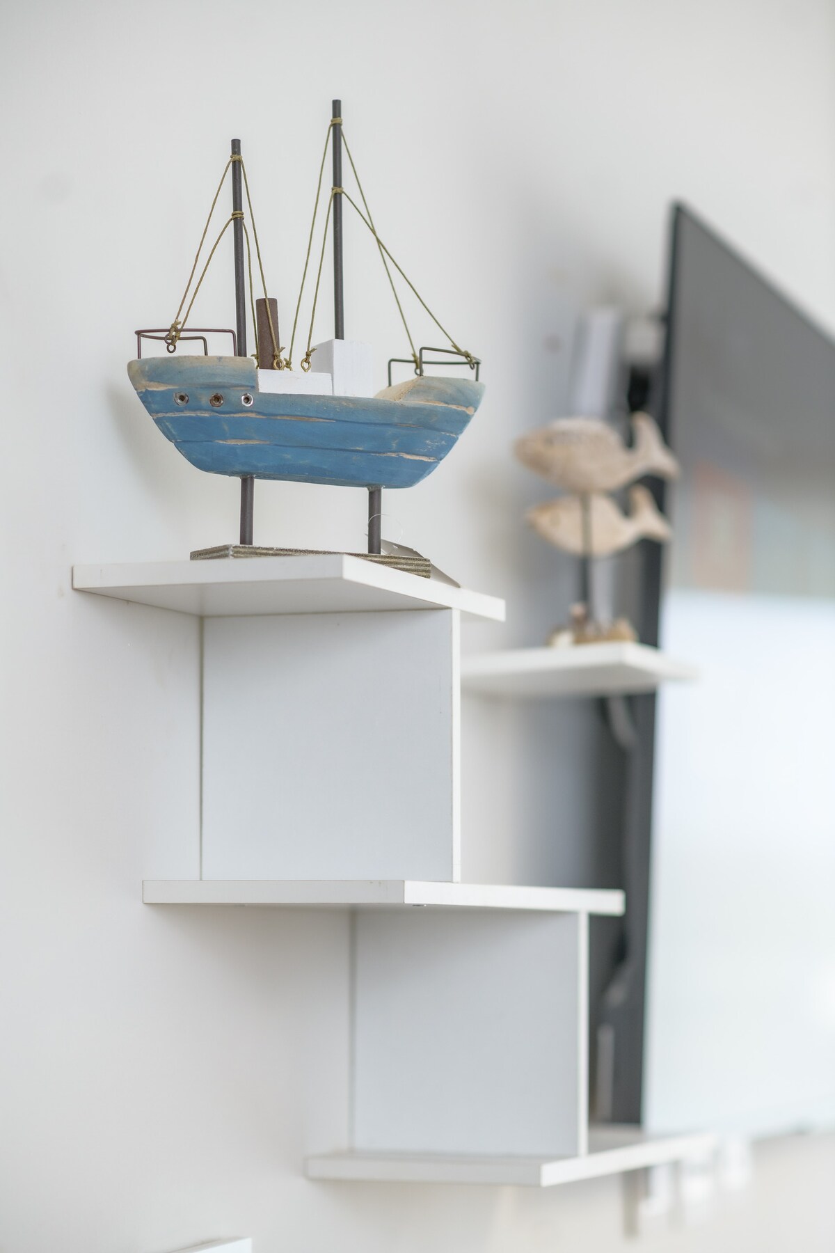 A decorative shelf features a small blue model ship alongside a fish statue. The shelves are mounted elegantly on a light-colored wall, contributing to a clean and organized look in the living space.