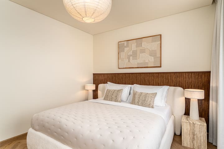 Chumba cha kulala cha kimtindo kilicho na kitanda cha starehe, fanicha za kisasa na madirisha ya sakafu hadi dari yanayotoa mandhari ya kupendeza ya jiji, mchana na usiku.