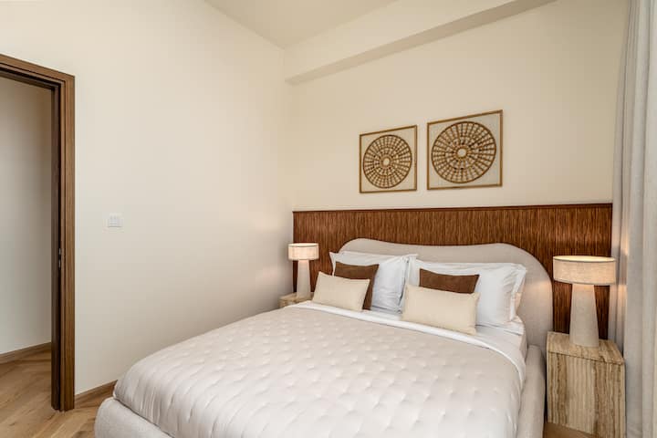 Chumba cha kulala cha kimtindo kilicho na kitanda cha starehe, fanicha za kisasa na madirisha ya sakafu hadi dari yanayotoa mandhari ya kupendeza ya jiji, mchana na usiku.