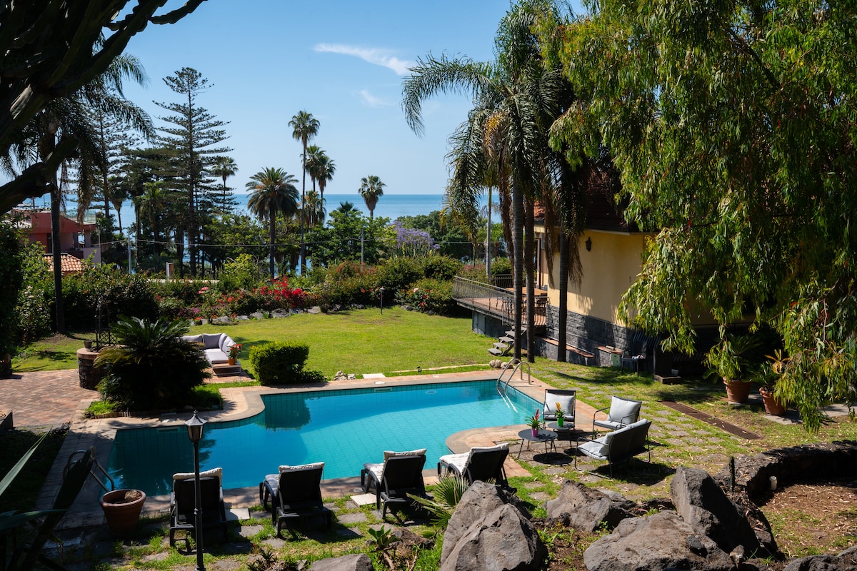 A spacious outdoor area features a private swimming pool surrounded by sun loungers, offering views of lush greenery and coastal scenery. Nearby tropical plants and palm trees create a serene atmosphere, enhancing the sense of privacy in this inviting garden space.