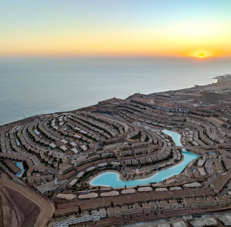 A panoramic view captures the coastline and resort layout, highlighting serene water features and organized housing clusters. Soft sunlight bathes the scene at sunset, creating a tranquil atmosphere over the expansive beach and horizon.