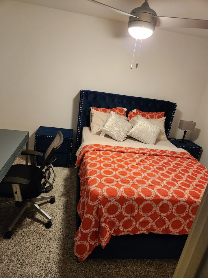 Dormitorio uno con escritorio, silla, dos mesitas de noche, dos lámparas y una cama tamaño queen. 
