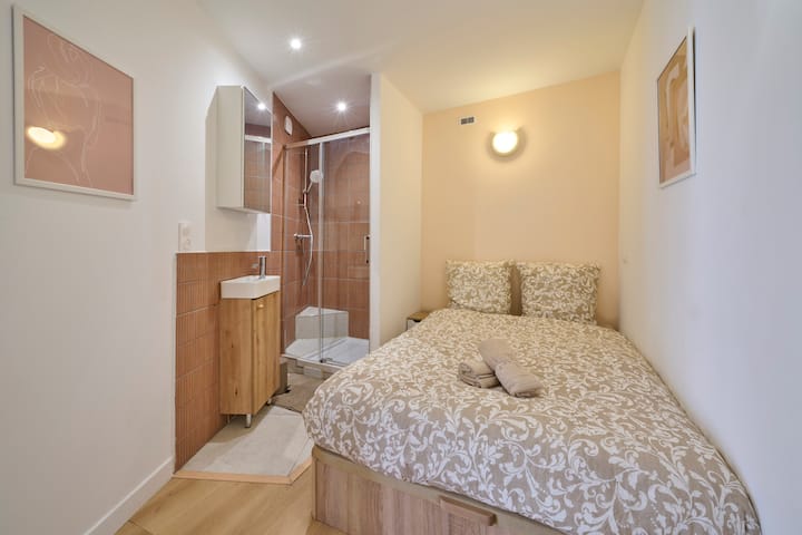 מפלס נמוך יותר: חדר נוח עם מיטה זוגית 140x190 ס"מ, מצעים מעוצבים וחדר רחצה פרטי עם מקלחת, כיור ואחסון. מרחב אינטימי ופונקציונלי לשהייה נוחה.