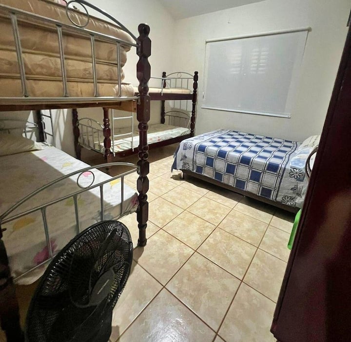 Chambre 2 avec un lit double, deux lits superposés, des rideaux occultants, de l'espace pour ranger des vêtements et du linge de maison, y compris des couvertures et des oreillers supplémentaires et un ventilateur portable.