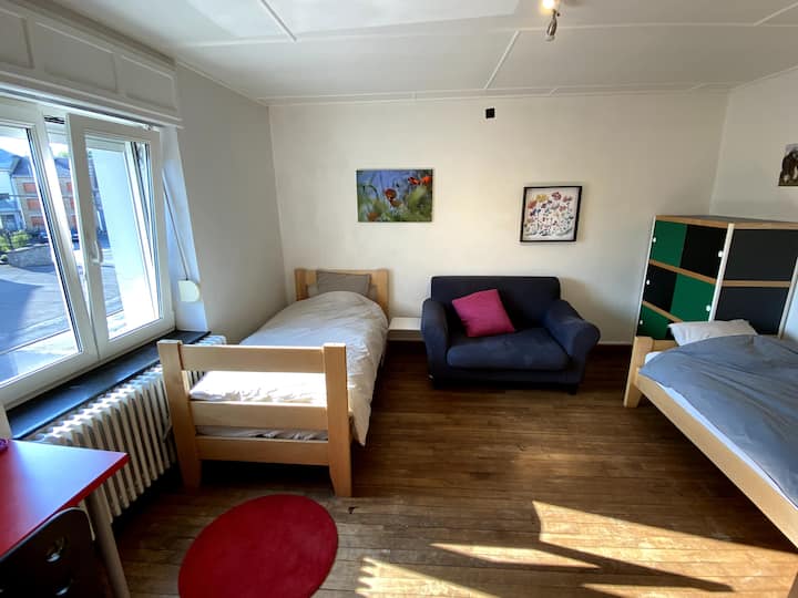 Dos camas con una mesa, una silla, un sillón y dos armarios. Una cama plegable para bebés también se encuentra en la habitación.