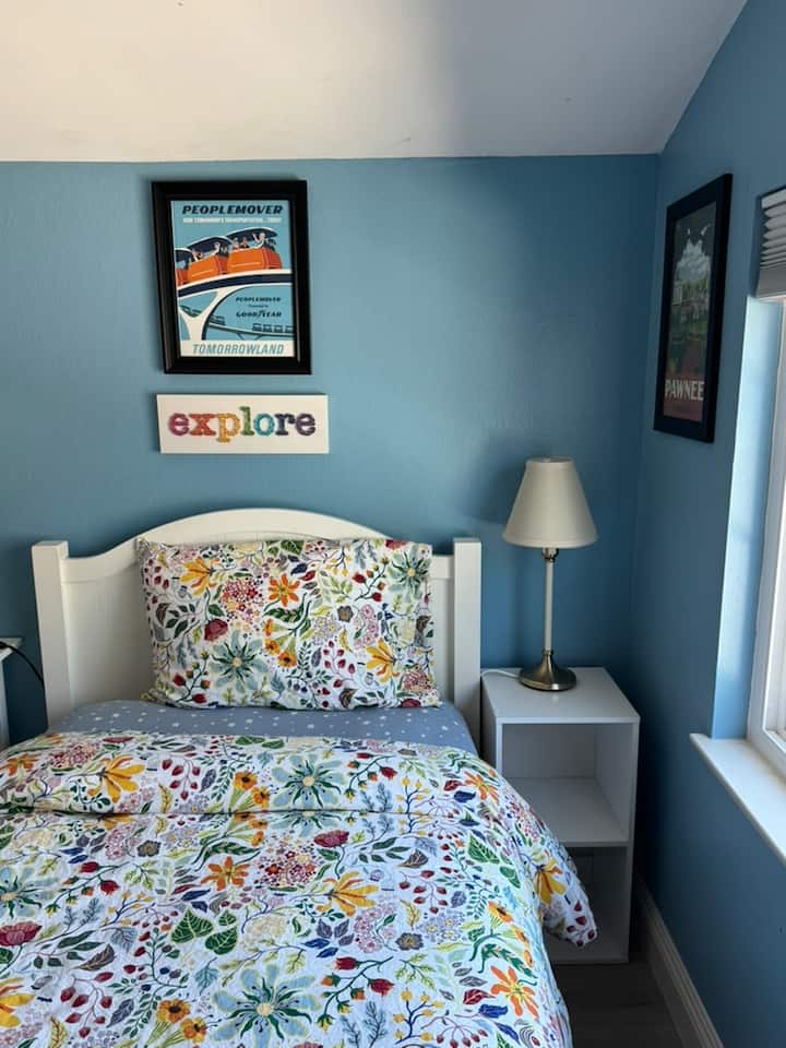 Bright twin bed setup with cheerful bedding, a comfy pillow, nightstand and lamp for reading, and playful travel-themed wall art to make the space feel uplifting and personal.