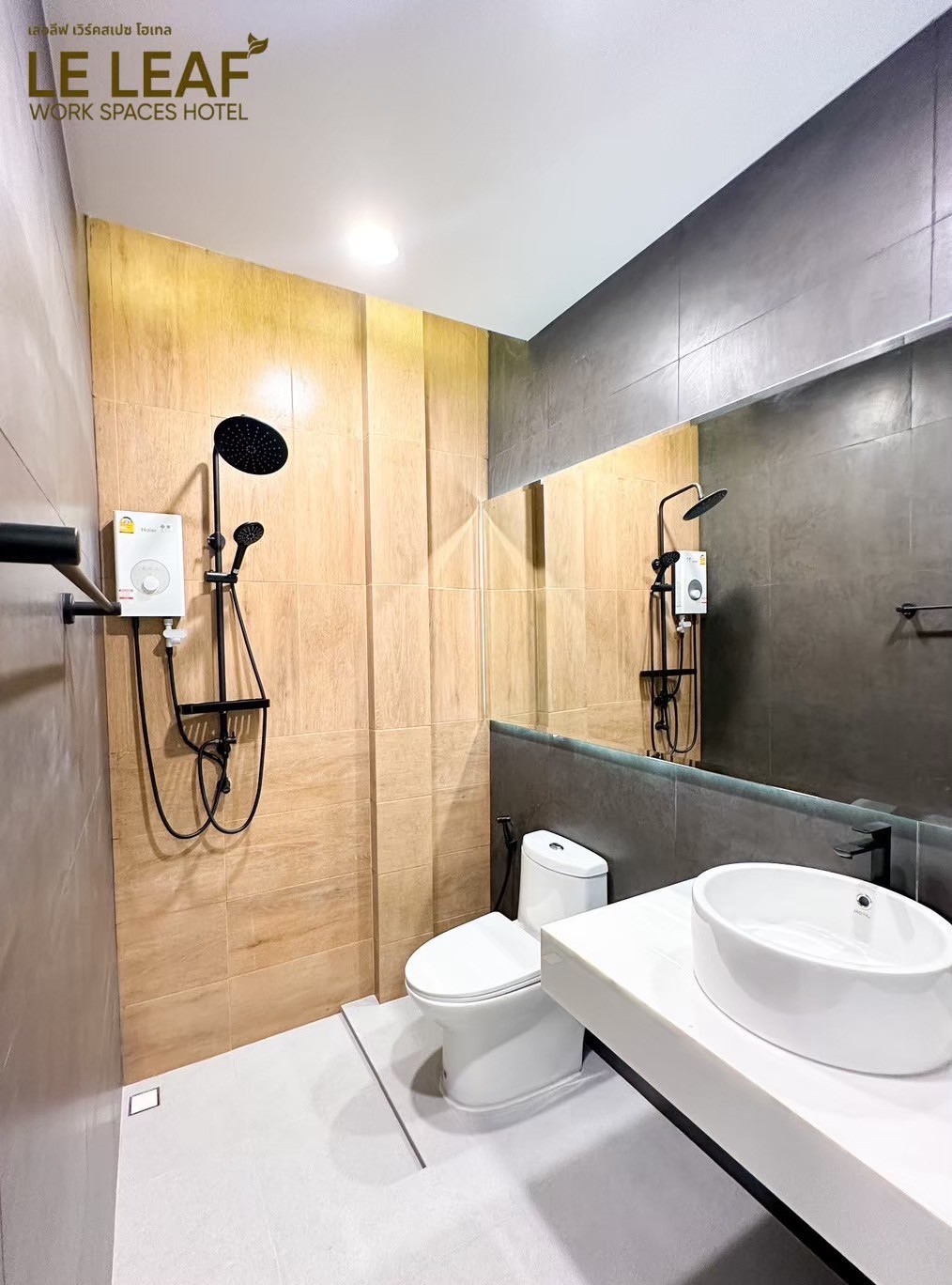 The bathroom features a modern design with a wooden accent wall and sleek fixtures. A round sink is positioned on a spacious countertop, complemented by a toilet and a shower area with a rain shower head. Neutral tones create a clean and refreshing ambience.