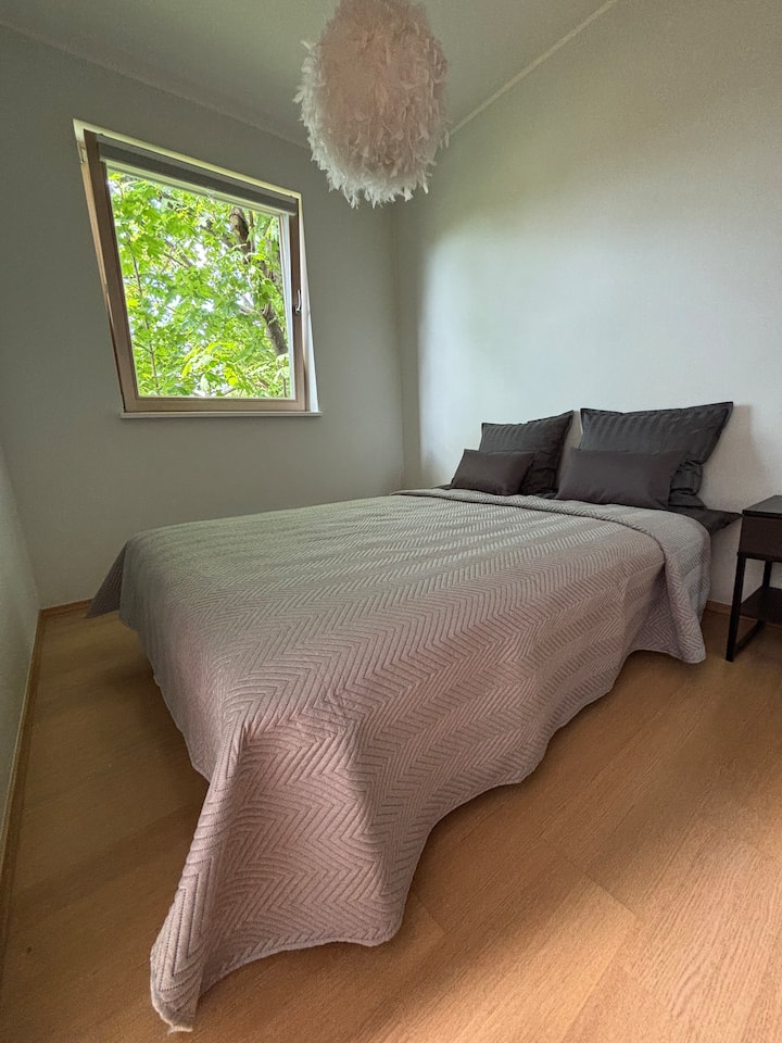 Cozy bedroom with a comfortable double bed and soft bedding. The window overlooks lush greenery, creating a calm and private atmosphere for a restful stay.