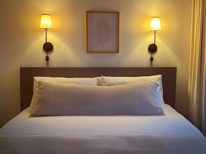 Relájate en una acogedora cama tamaño king enmarcada por una iluminación suave y tonos tranquilos y terrosos. El cálido resplandor de los apliques crea un ambiente tranquilo, perfecto para leer o descansar después de un día en la ciudad. Si tienes alguna pregunta, estoy a tu disposición.