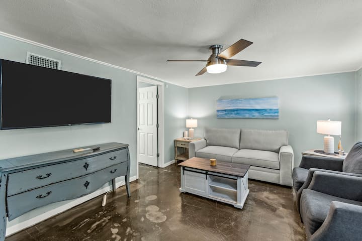Downstairs living room with a large TV, comfortable seating, and coastal touches. A perfect spot to unwind, stream your favorite shows, or enjoy family time.
