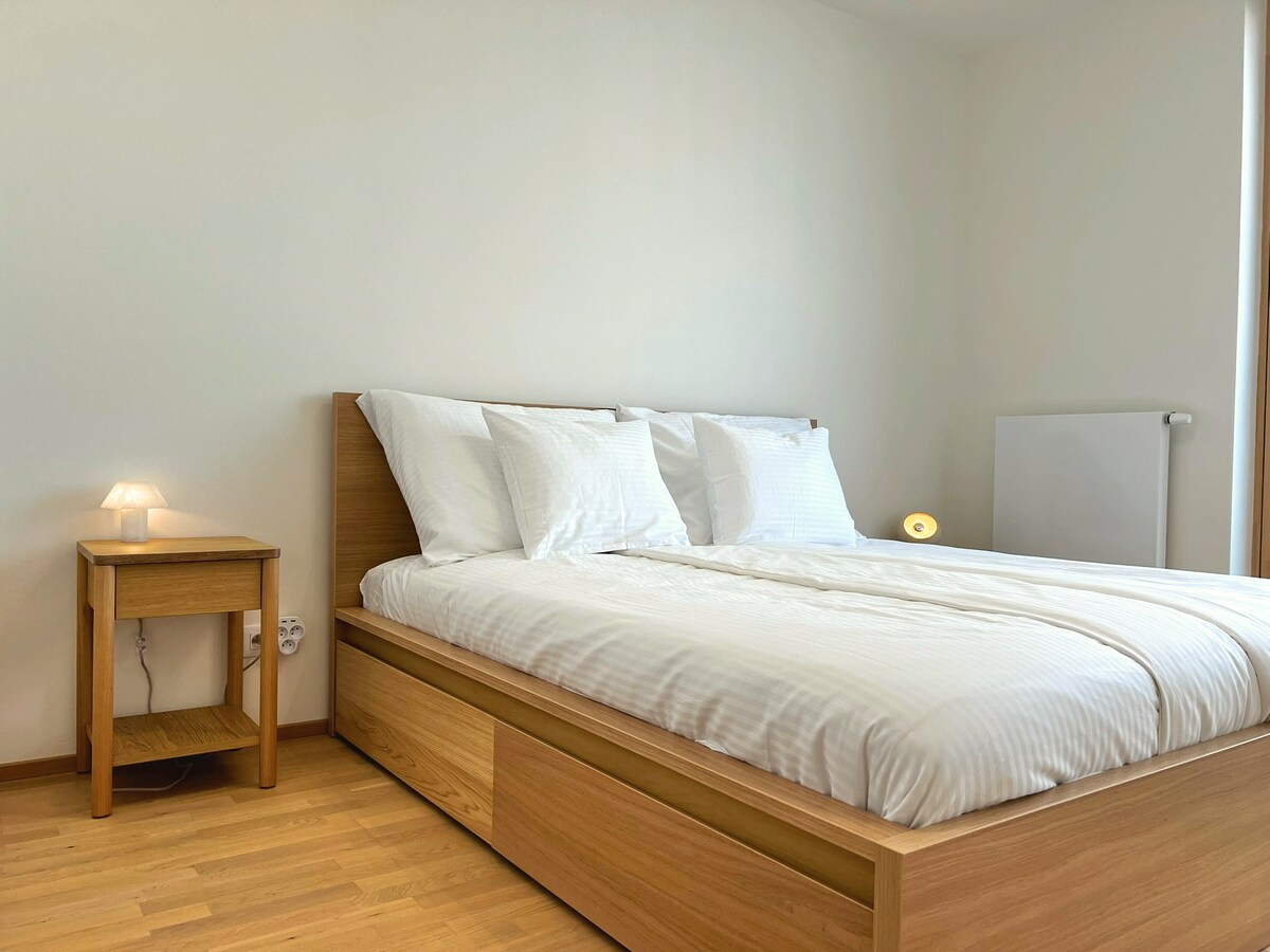 Manželská posteľ s nadštandardnou posteľnou bielizňou z bavlny Kvalitex, plyšovými vankúšmi a nočnými lampičkami – váš osobný oddychový priestor na pokojné noci.